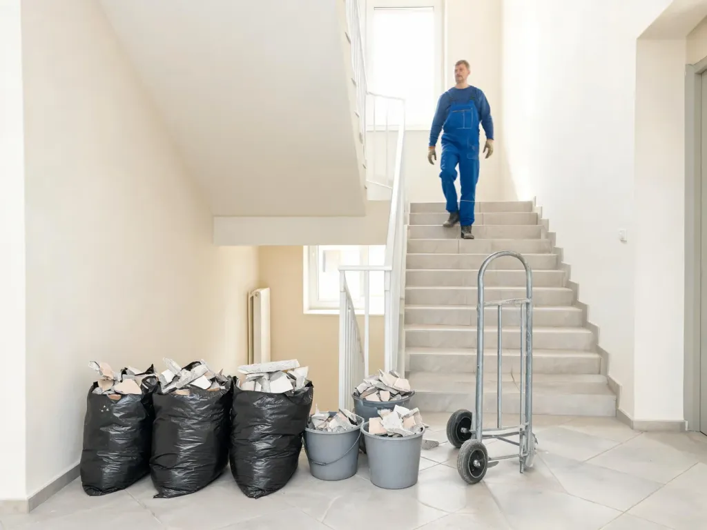 Workman znoszący po schodach worki z gruzem i wiadra z odpadami, ilustrujący wynoszenie gruzu z mieszkania